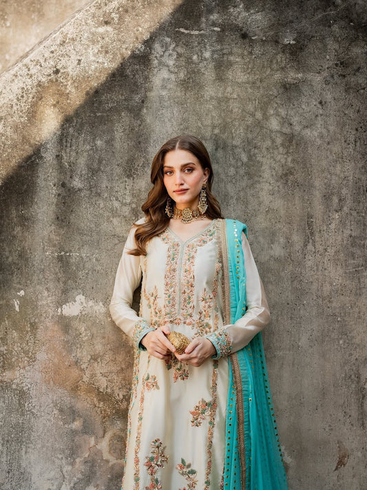 Woman in elegant cream ethnic dress with intricate embroidery and blue dupatta against textured wall