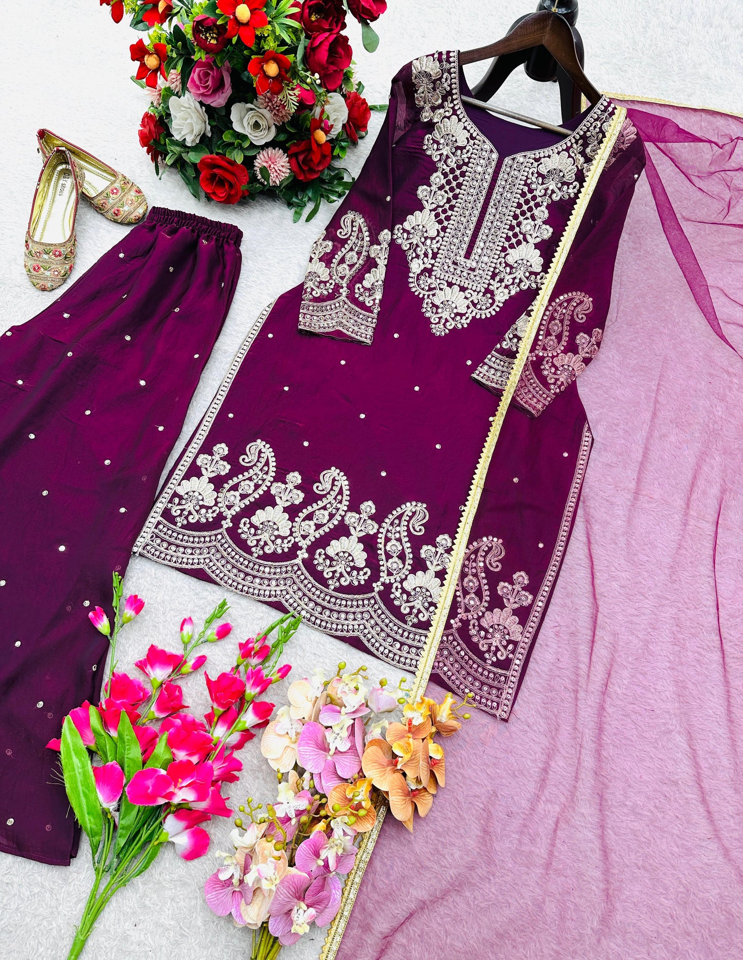 Purple embroidered ethnic women's salwar kameez set with matching pants, dupatta, traditional shoes, and vibrant flower bouquets