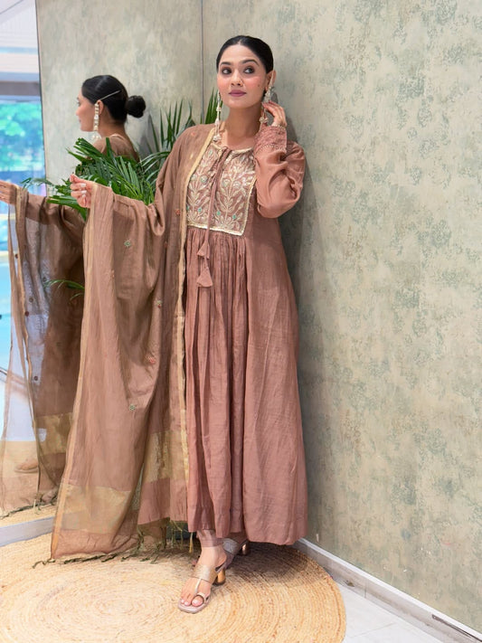 Front view of full three piece rosy brown ethnic suit showcasing an embroidered A line Anarkali flared kurti and matching trousers.