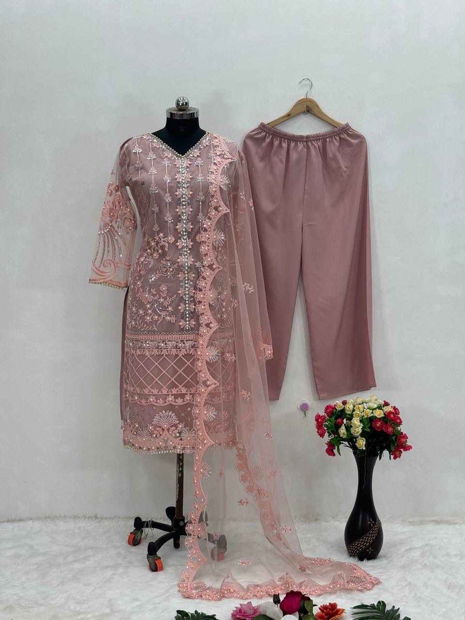 Close up view of detailed chine sequence patterns and shimmering pearl hand work decorations on soft dusty rose net fabric.