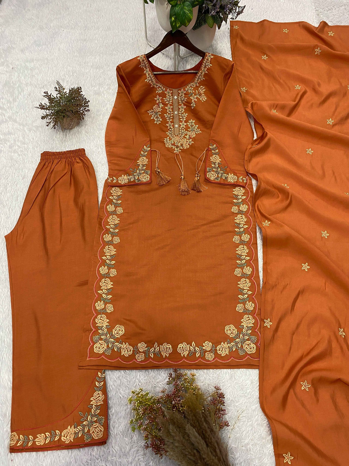 Close up view of detailed ethnic embroidery thread work and matching hanging latkan details on a rust orange roman silk neckline.