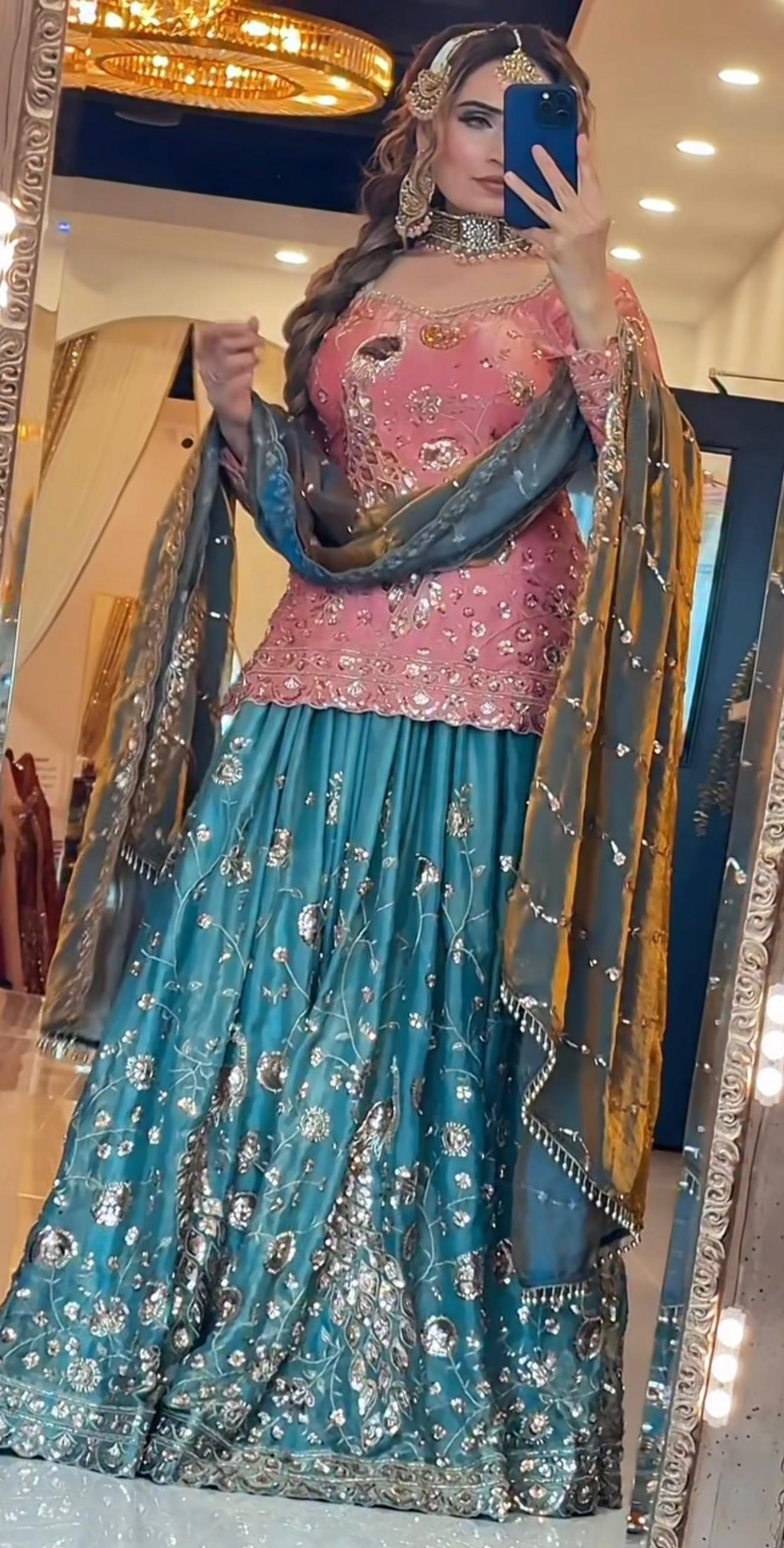 Front view of full three piece coral pink traditional party wear outfit showcasing an embroidered crushi silk top tunic and matching wide leg sharara pants.