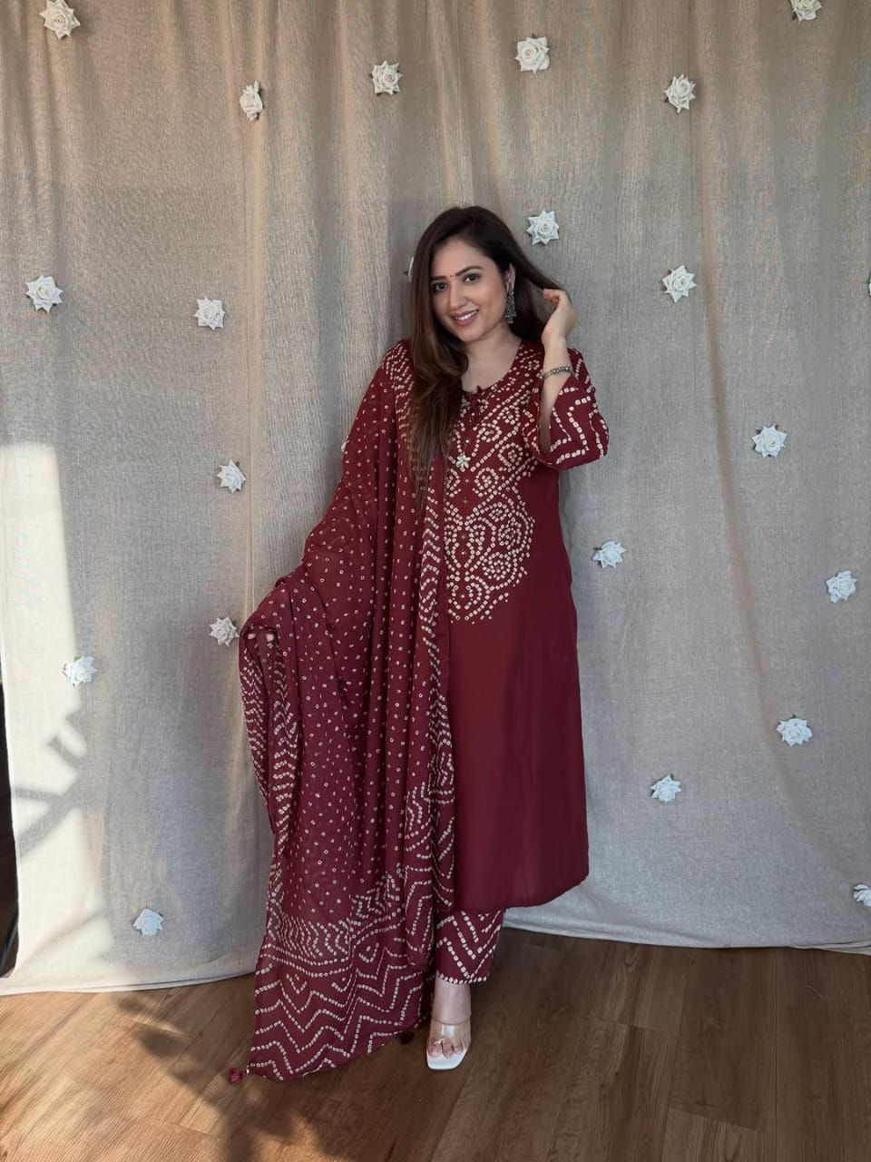 Front view of full three piece wine color traditional ethnic outfit displaying an all over bandhani discharge printed kurta straight trousers and matching cotton dupatta.
