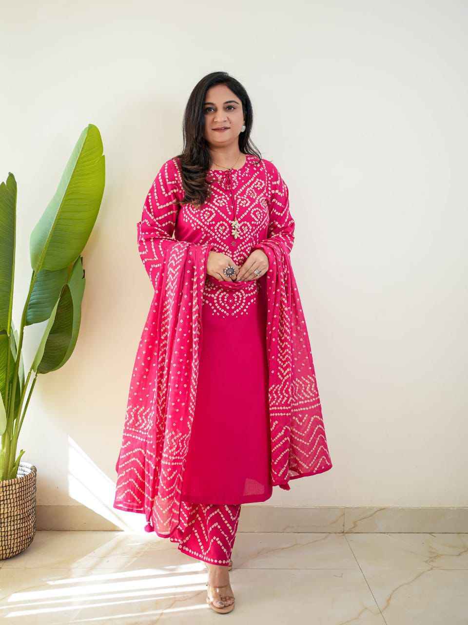 Front view of full three piece dark pink traditional ethnic outfit displaying an all over bandhani discharge printed kurta straight trousers and matching cotton dupatta.