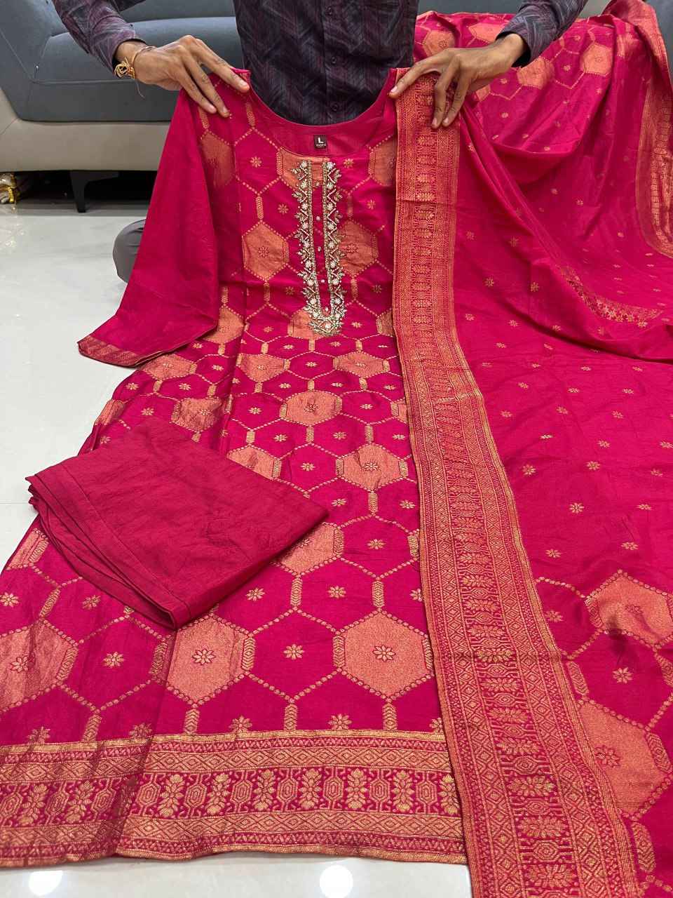 Pure BanarasiClose up view of detailed traditional handwork neck embroidery and premium gold zari weaving patterns on a dark pink banarasi fabric bodice.Jacquard Suit Set