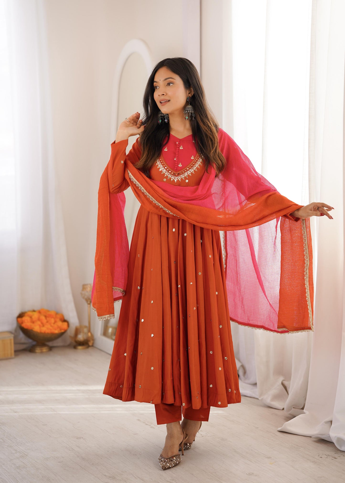 Front view of a rich vibrant orange traditional three piece suit displaying a heavily embroidered long anarkali gown and matching straight trousers.