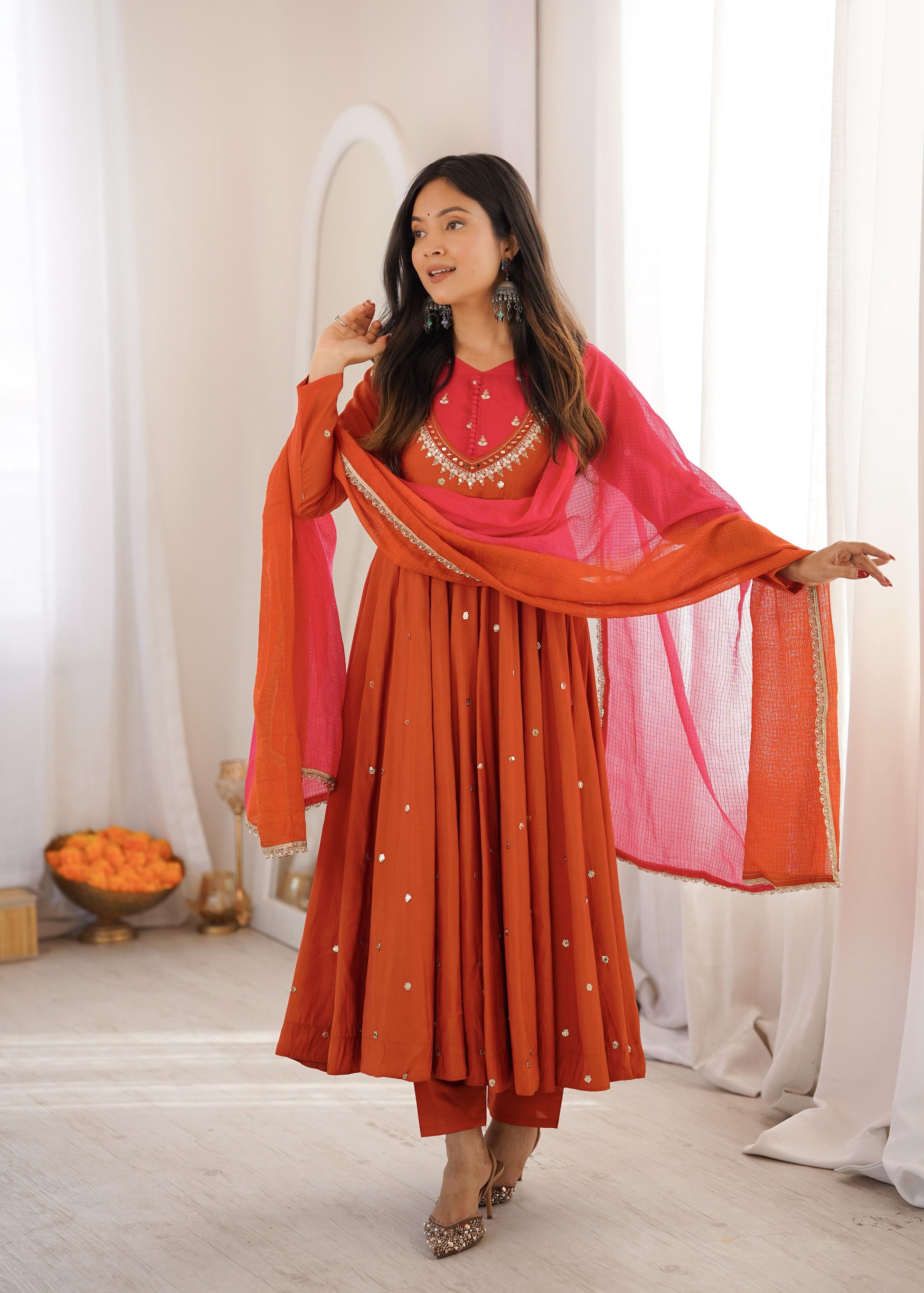 Front view of a rich vibrant orange traditional three piece suit displaying a heavily embroidered long anarkali gown and matching straight trousers.